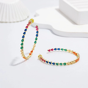 Golden hoop earrings with colorful pear-cut zircon stones on a white stand