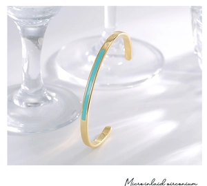Detailed macro view of the gold open bangle with micro-inlaid zirconium and blue enamel