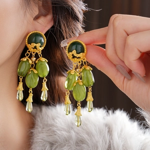 Detail of vintage gold earrings with green gemstones and elegant beaded tassels