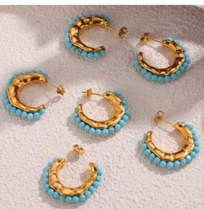 Detail showing golden C-shaped stud earrings with turquoise blue beads on stone surface