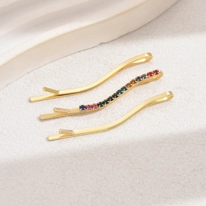 Dettaglio di tre forcine dorate a forma di S con strass colorati e motivi a onde