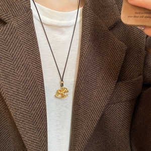 Close-up of golden rocking horse pendant with brown necklace cord on a tweed jacket