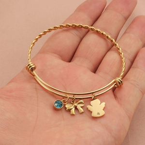 Gold titanium steel twist bangle with angel charm, blue gemstone, and bow pendant