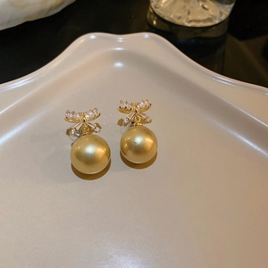 Detailed close-up of gold bow earrings with round pearls and sparkling cubic zirconia