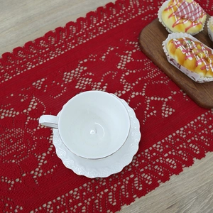 Red lace knitted Christmas table runner on a wooden surface with a cozy tea setting