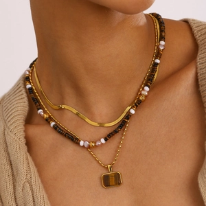 Detailed view of layered gold snake chain and beaded necklace with tiger eye stone pendant
