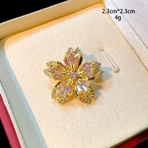 Détail macro d'une broche fleur dorée de 2,3 cm avec pierres roses en boîte à bijoux