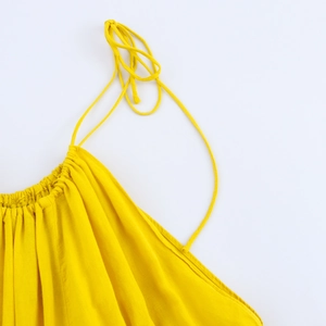 Detail of yellow backless summer dress featuring thin straps and pleated neckline texture