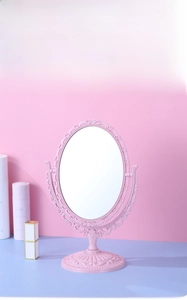 Detail of pink retro desk makeup mirror with ornate floral embossed frame and oval glass