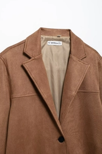 Detail of brown suede blazer collar featuring a white woven size label and black button