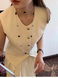 Detail of layered pearl necklaces with golden accents and black square pendants on model