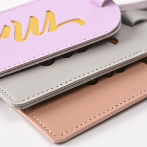 Close-up of three PU leather luggage tags in lavender, light grey, and soft pink tones