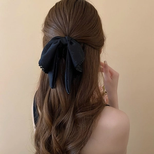 Detail of large black bow hair claw clip with pearl beaded edges and glitter finish