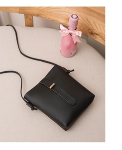 Detail of minimalist black leather mini crossbody bag with golden hardware and strap knots