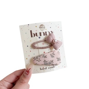 Pink floral and bowknot hair clip set for kids on a card held by a hand in white background