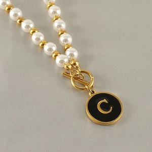 Détail du collier en or 18k avec perles et pendentif rond noir orné de la lettre C