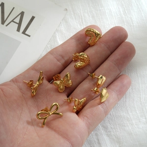 Golden stud earrings set with butterfly and heart shapes shown on palm for size reference