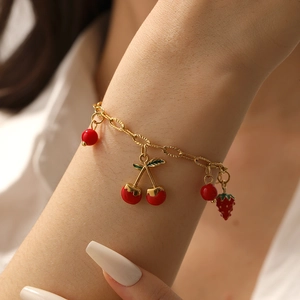 Détail d'un bracelet doré avec des breloques émaillées cerise et fraise rouges au poignet