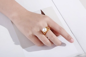 Close-up of a large white pearl ring with diamond accents on a golden titanium band