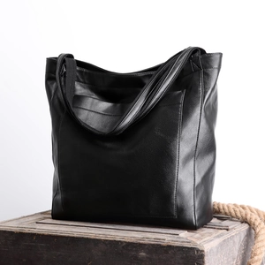 Détail du sac cabas en cuir ciré noir au style vintage posé sur un coffre en bois rustique