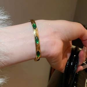 Detail of a gold-plated open bracelet with three marquise-cut green gemstones on a model