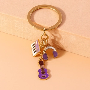 Detail of musical charms featuring purple piano, headphones, and ukulele on gold keychain