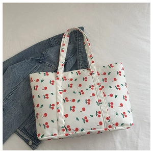 Close-up of white canvas tote bag with red cherry print and long shoulder straps