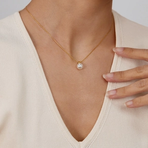 Detail showing an elegant white pearl pendant on a thin golden stainless steel necklace