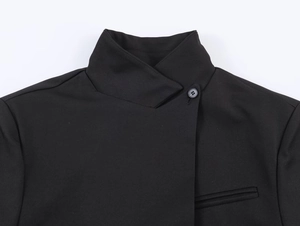 Detail of black blazer with stand collar, asymmetric front, and circular button closure