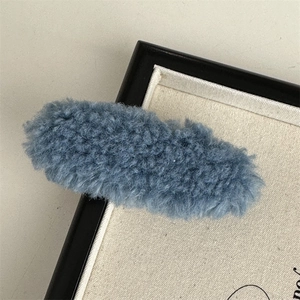 Close-up of a blue plush faux shearling hair clip displayed in a black frame