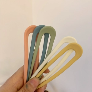 Hand holding five colorful U-shaped hairpins in soft Morandi candy tones for styling