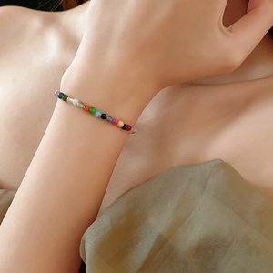 Detailed view of a colorful beaded bracelet worn on a wrist against a green fabric