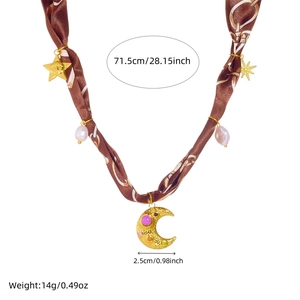 Détail du collier en soie avec breloques lune, étoile dorées et perles sur fond blanc