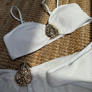Macro detail of ribbed white bikini fabric and textured gold metal buckle accent