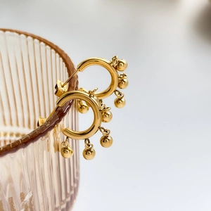 Macro shot of gold hoop earrings with polished beads hanging on a textured glass rim
