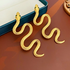 Macro shot of gold snake earrings with green gem eyes and detailed scale texture