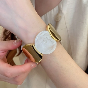 Détail d'un bracelet doré épais avec disques en résine marbrée blanche sur un poignet