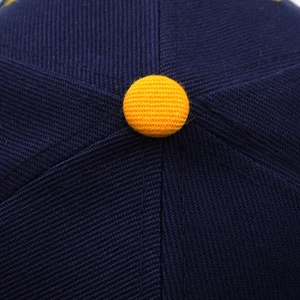 Macro shot of navy blue cotton baseball cap crown with contrast yellow top button detail