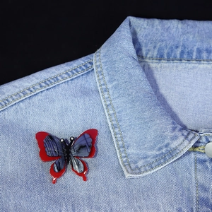 Artistic acrylic butterfly brooch with marble blue and red wings pinned on denim jacket