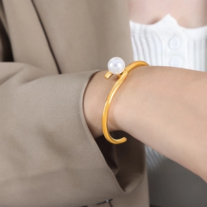 Chic gold-plated S-shape open cuff bracelet with white pearl on a model's wrist