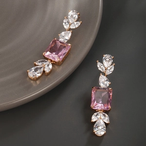 Detail of gold earrings featuring pink rectangular zircon and white teardrop stones