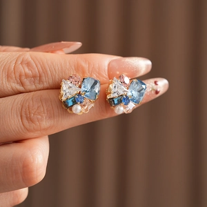 Detailed close-up of geometric earrings with colorful zircons and pearls held by hand