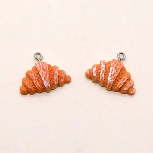 Close-up of resin croissant pendants with white icing detail and metal loops