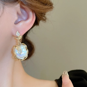 Gros plan d'une boucle d'oreille en perle baroque dorée avec feuilles de zircon