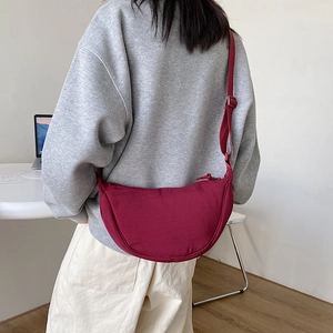 Close-up of red nylon dumpling crossbody bag worn by a model in a minimalist setting