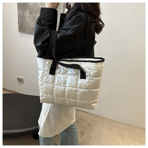 Close-up of white quilted tote bag with black strap worn by a model in leather jacket