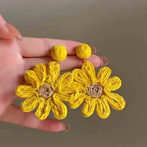 Detailed view of handmade yellow woven flower earrings with brown cord centers