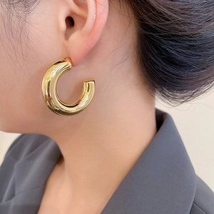 Close-up of model wearing thick gold C-shaped hoop earrings with polished finish
