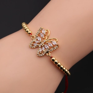 Macro shot of a butterfly zircon pendant with gold beads on a red braided bracelet