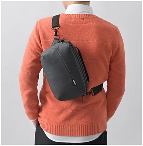 Rear view of a grey waterproof men's crossbody bag on a casual orange sweater